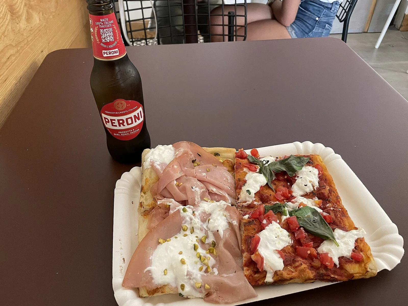 Due tranci di pizza al taglio, uno con mortadella e stracciatella e uno con pomodoro e basilico, serviti su un vassoio di carta a Roma